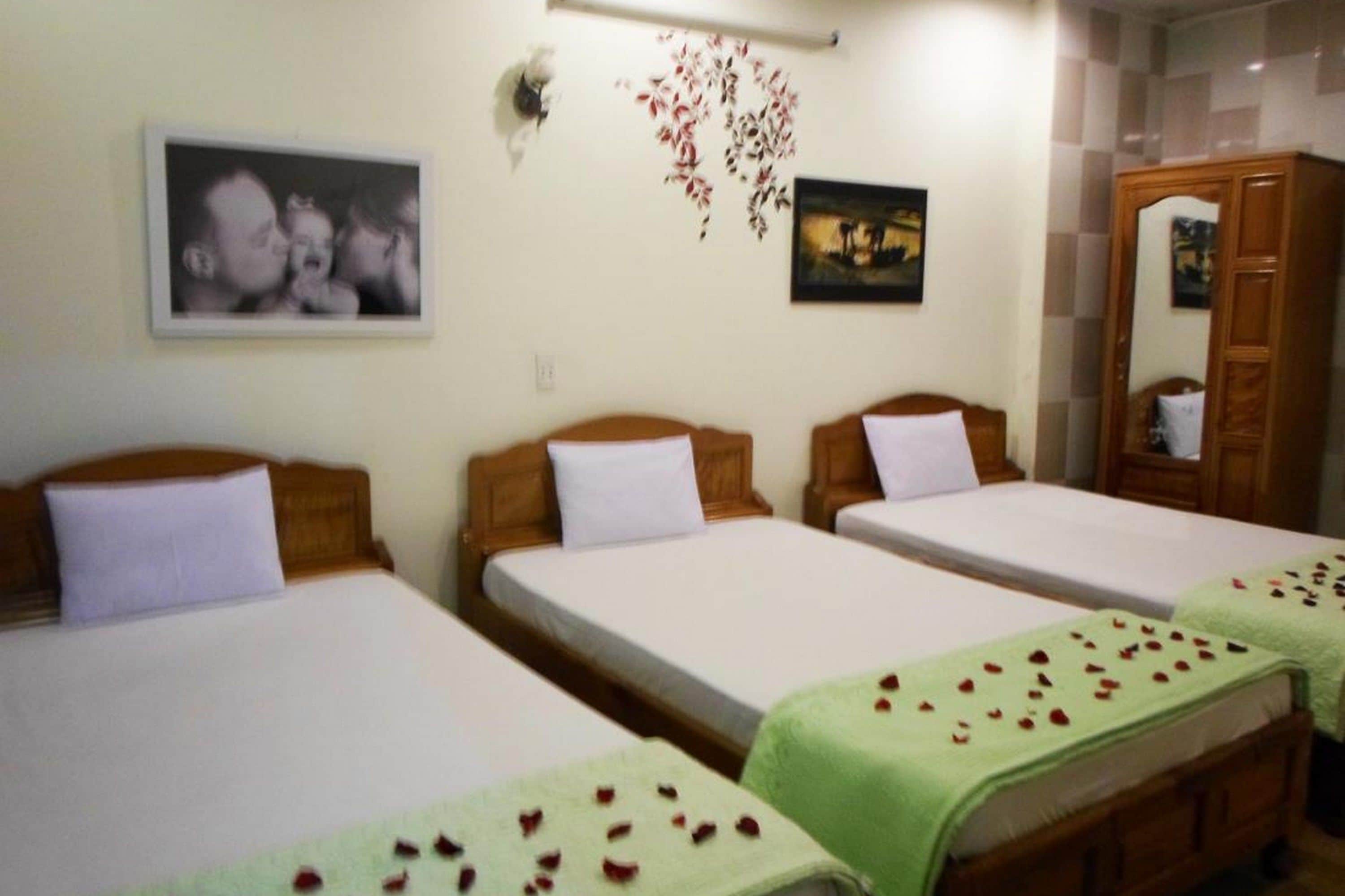 Ett hotellrum med tre enkelsängar, en garderob i trä och väggdekorationer, inklusive ett inramat fotografi och ett blommönster.