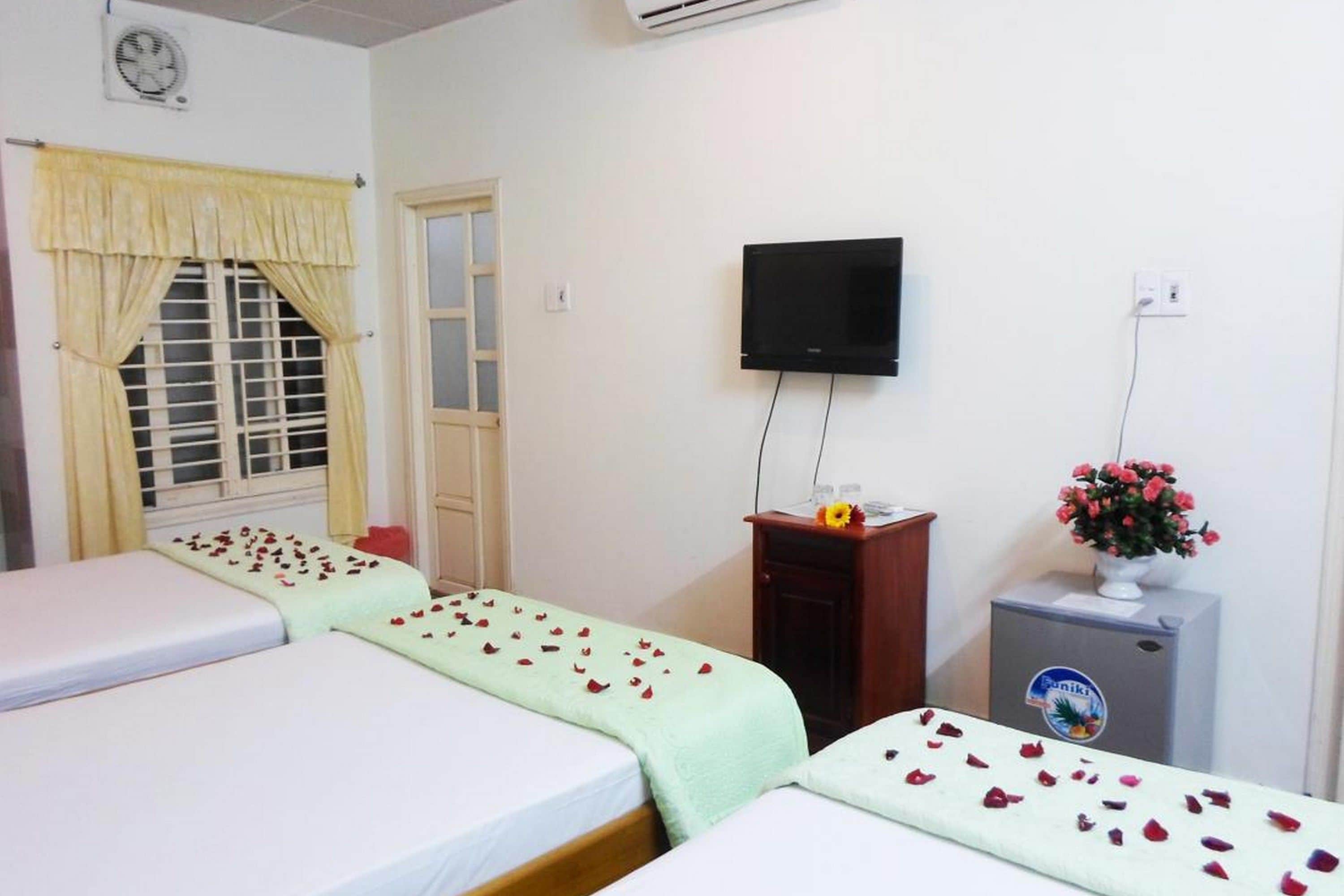 A hotel room with two beds, a television, a small desk, and a flower vase.