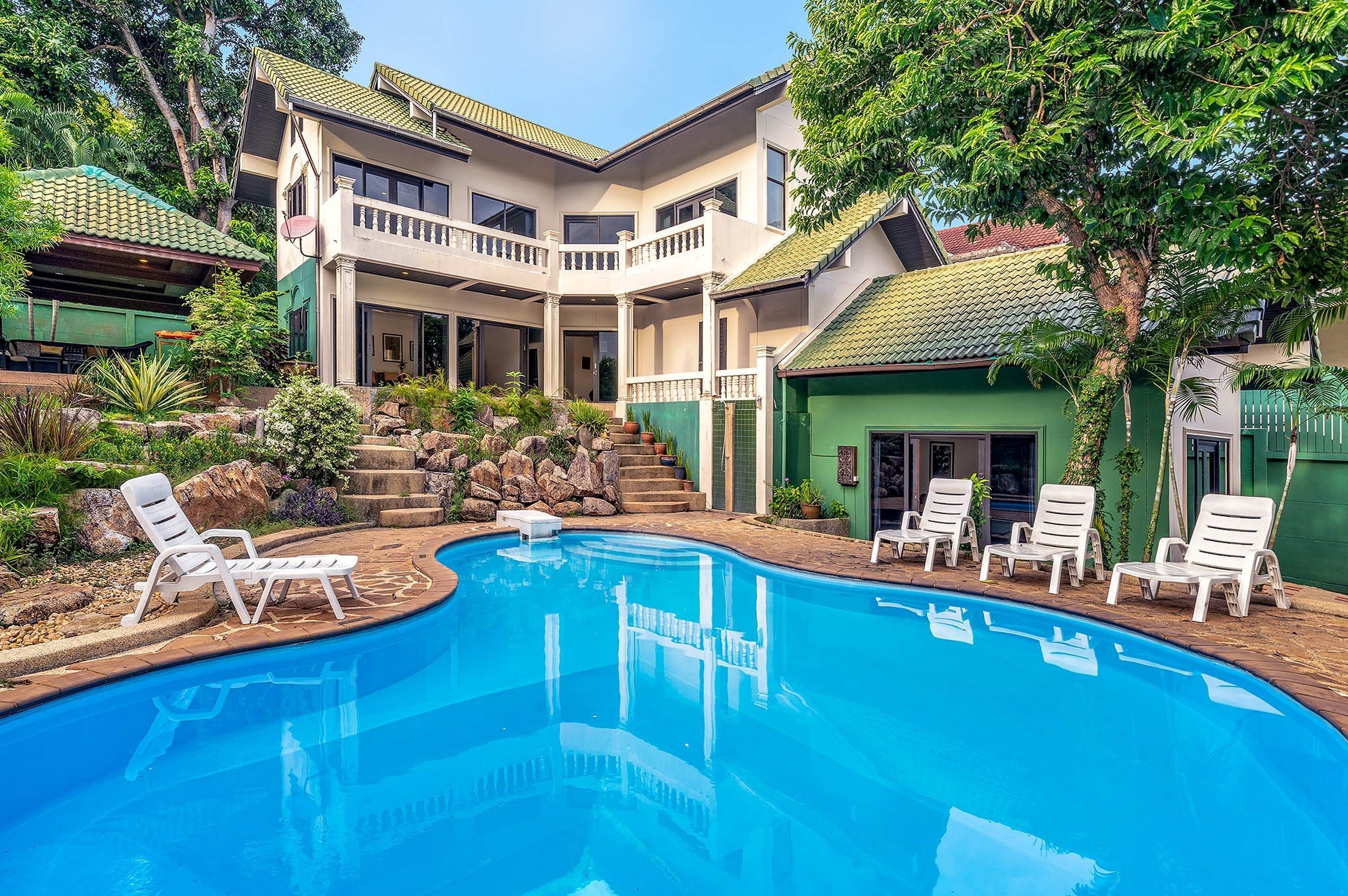 A two-story house with a swimming pool, surrounded by greenery and a small staircase.