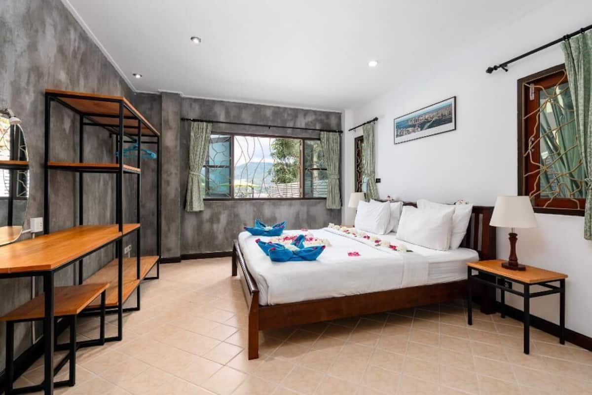 A bedroom with a bed, a desk, a lamp, and a window with curtains.