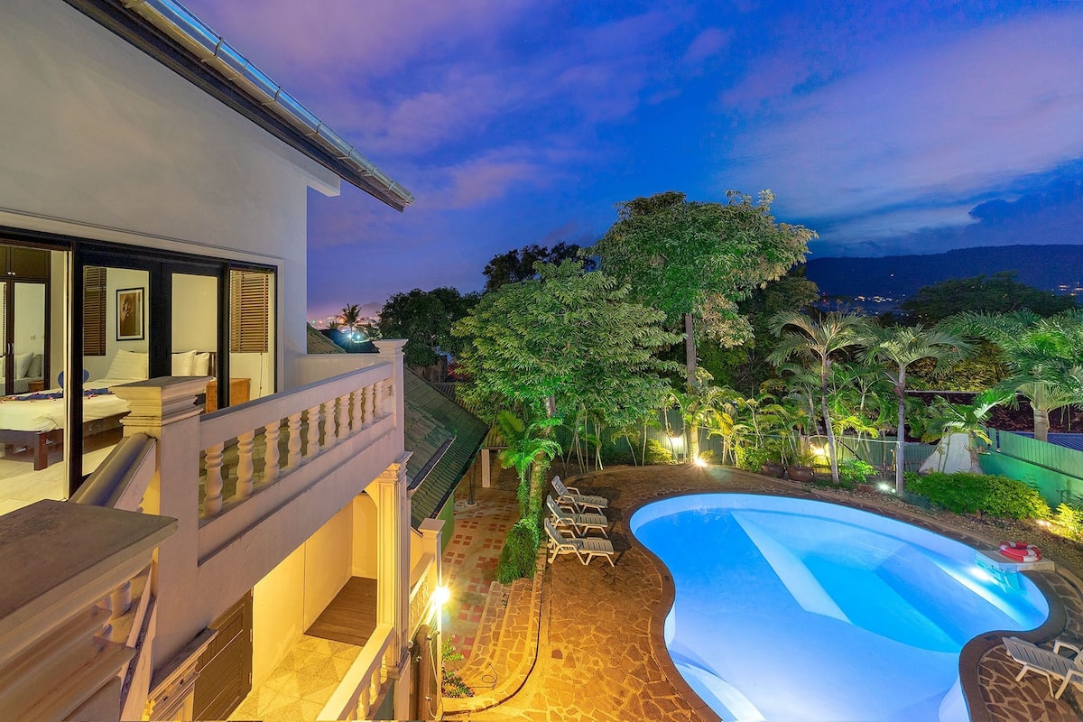 A modern house with a swimming pool, a balcony, and a view of the mountains.