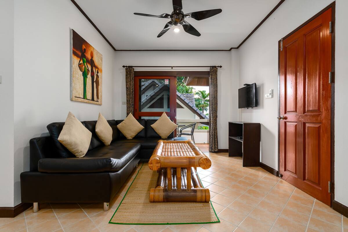 A living room with a black sofa, a wooden coffee table, a ceiling fan, and a door.