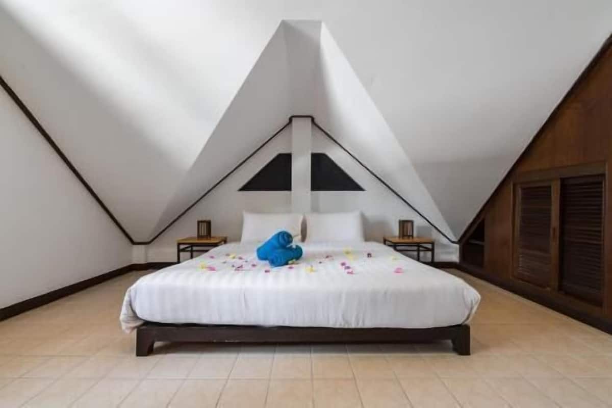 A bedroom with a sloped ceiling, a bed with white bedding, a blue pillow, and two bedside tables.