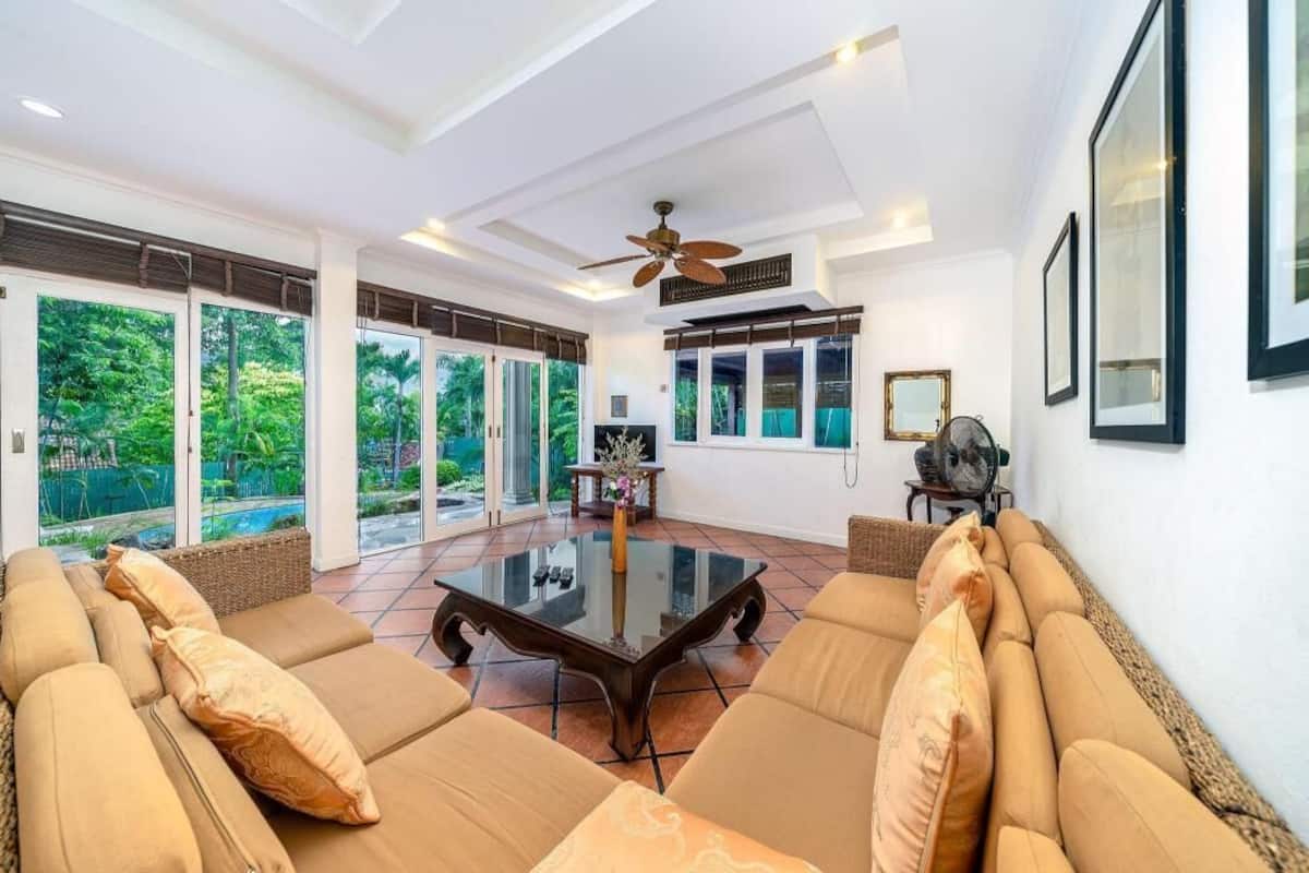 A spacious living room with a glass coffee table, beige sofas, and large windows offering a view of the outdoors.