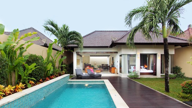 Una piscina con sillones de descanso, un patio cubierto y vistas al interior de una casa.