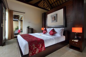 Quarto de hotel com uma cama grande, duas luminárias de cabeceira, uma mesa de apoio, uma obra de arte emoldurada acima da cama e vista através de uma porta aberta.