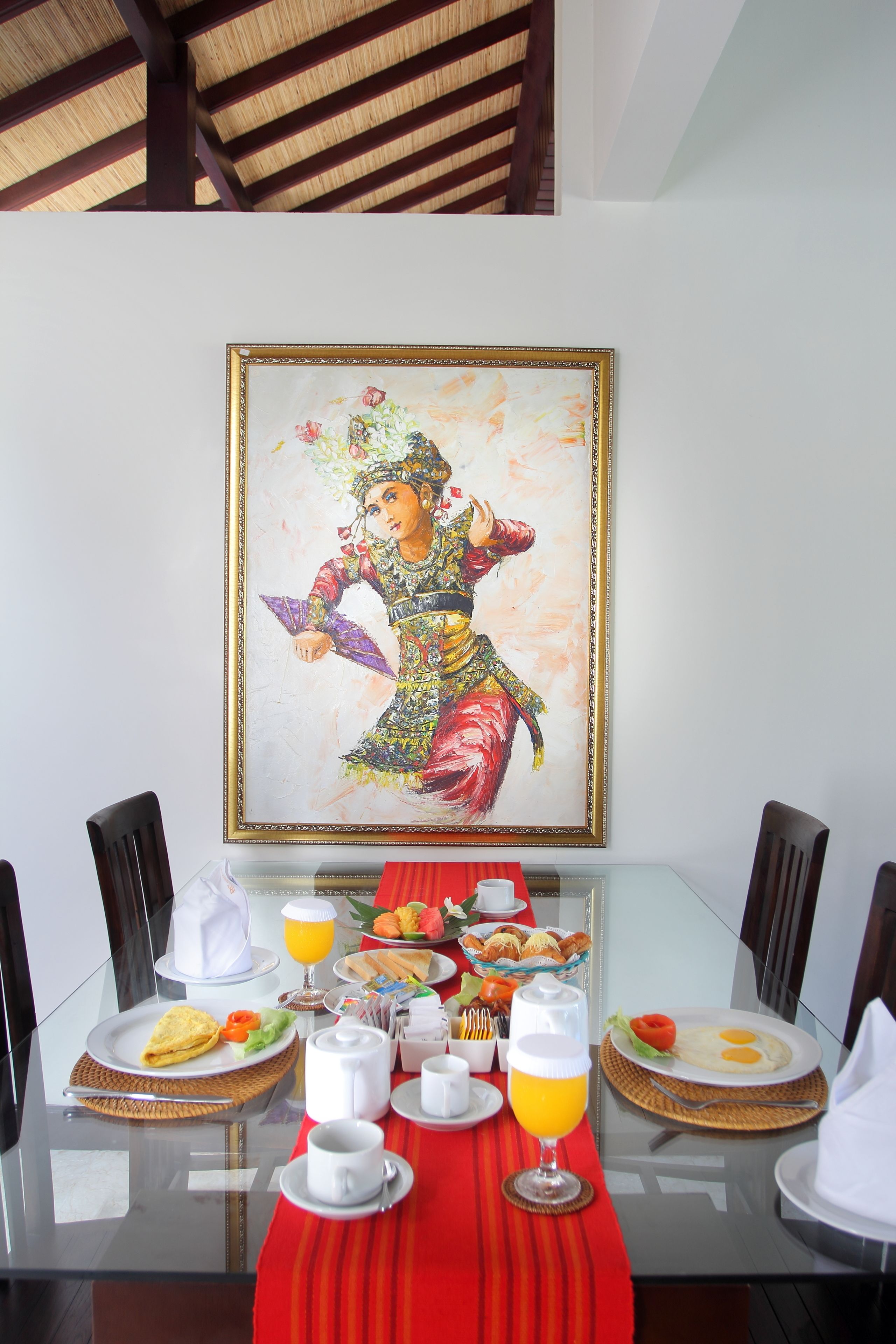 Een eettafel met ontbijtartikelen, een lijst met schilderij en een rode tafelkleed.