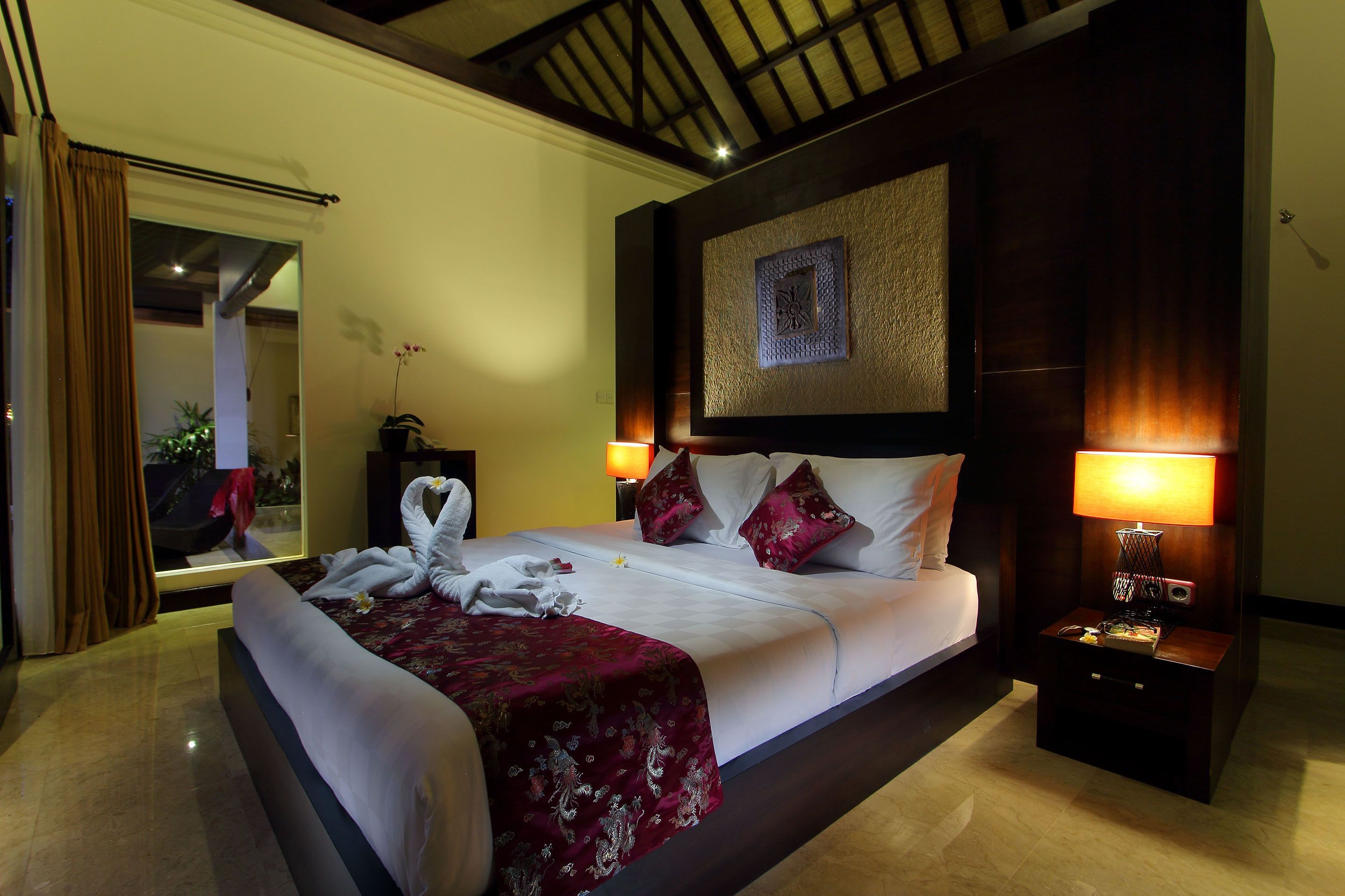 A hotel room with a large bed, two bedside lamps, a nightstand, and a view of the outdoors.