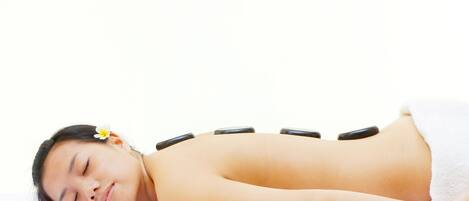 A person lying on a bed with a white towel, receiving a back treatment with black stones.