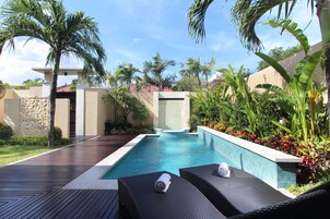 A pool area with two lounge chairs and a stone wall.