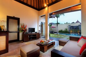 Una sala de estar moderna con televisor, sofá y mesa de centro. Se ve una piscina a través de la puerta de cristal.
