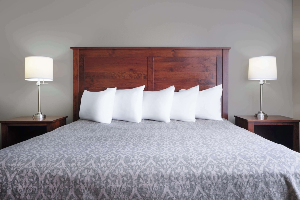 A neatly made bed with a patterned bedspread, flanked by two bedside tables with lamps, in a room with a wooden headboard.