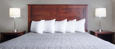 Una cama bien tendida con un edredón estampado, flanqueada por dos mesitas de noche con lámparas, en una habitación con cabecera de madera.