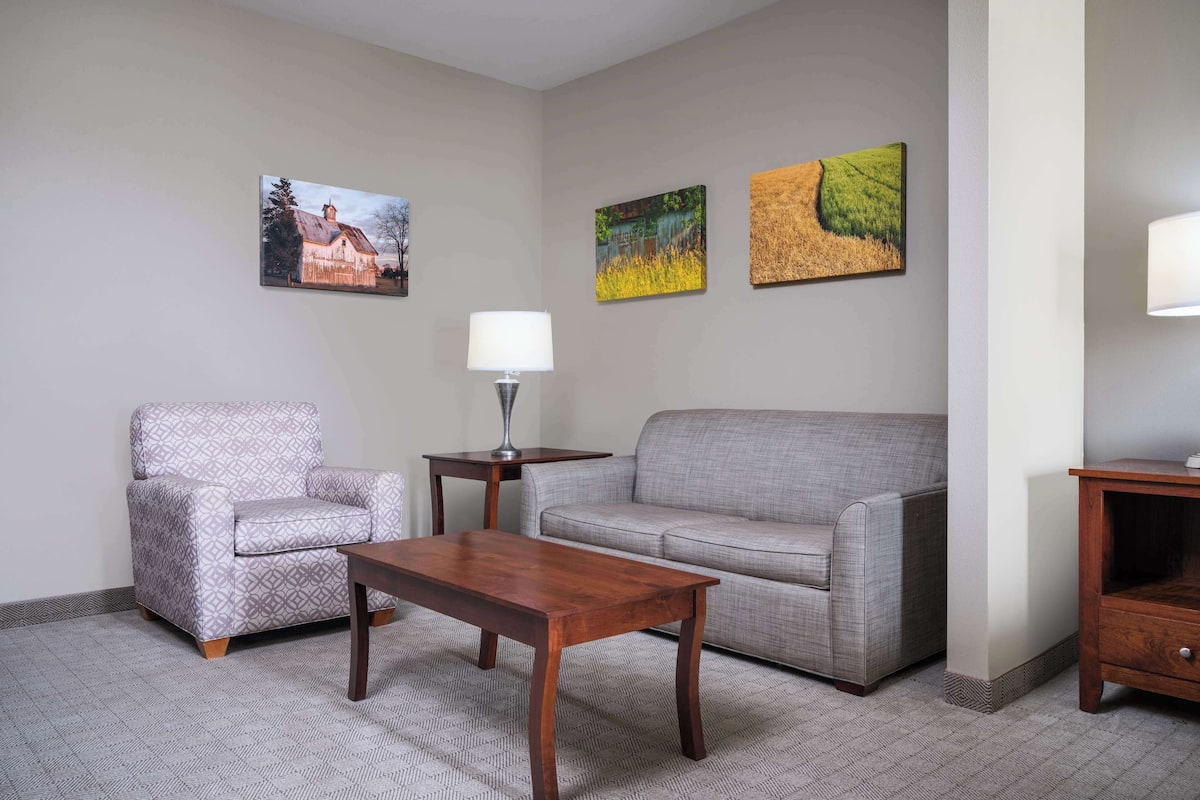 Una sala de estar con un sillón estampado, un sofá gris, una mesa de centro de madera y dos lámparas fijadas a la pared.