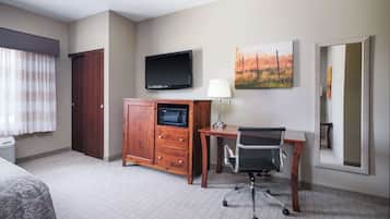 Una habitación de hotel con una cama, un escritorio con silla, televisor, microondas, lámpara y un espejo grande.