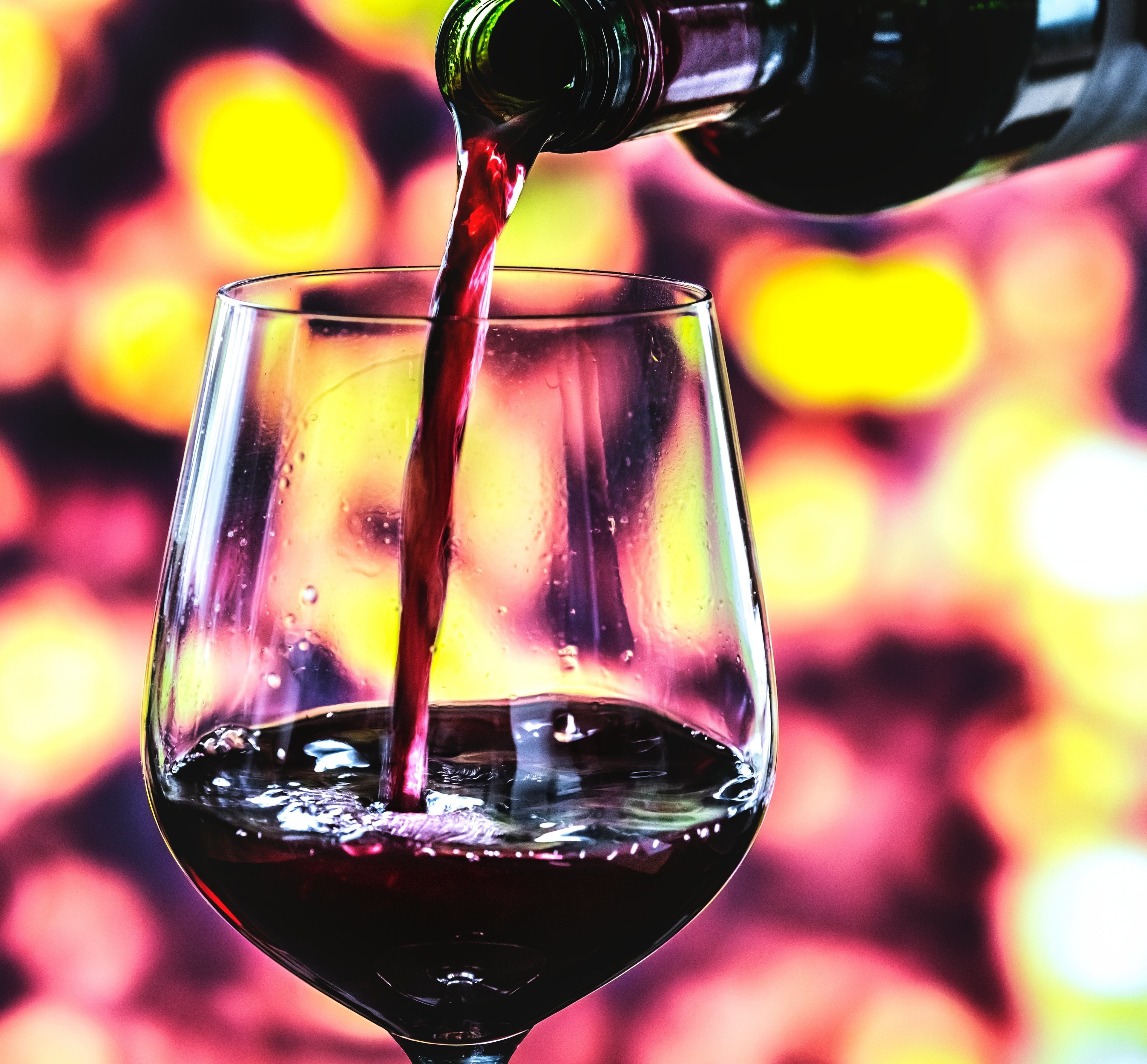 A glass being filled with red liquid, likely wine, against a blurred background with warm colors.