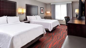 A hotel room with two beds, a desk, a chair, and a television.