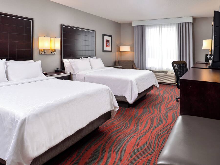 A hotel room with two beds, a desk, a chair, and a television.