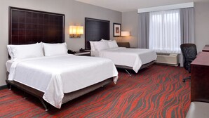A hotel room with two beds, a desk, a chair, and a large window with curtains.