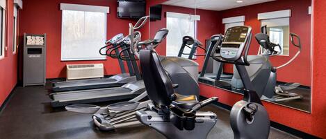 Un gimnasio con cintas de correr, elípticas y un televisor en la pared.