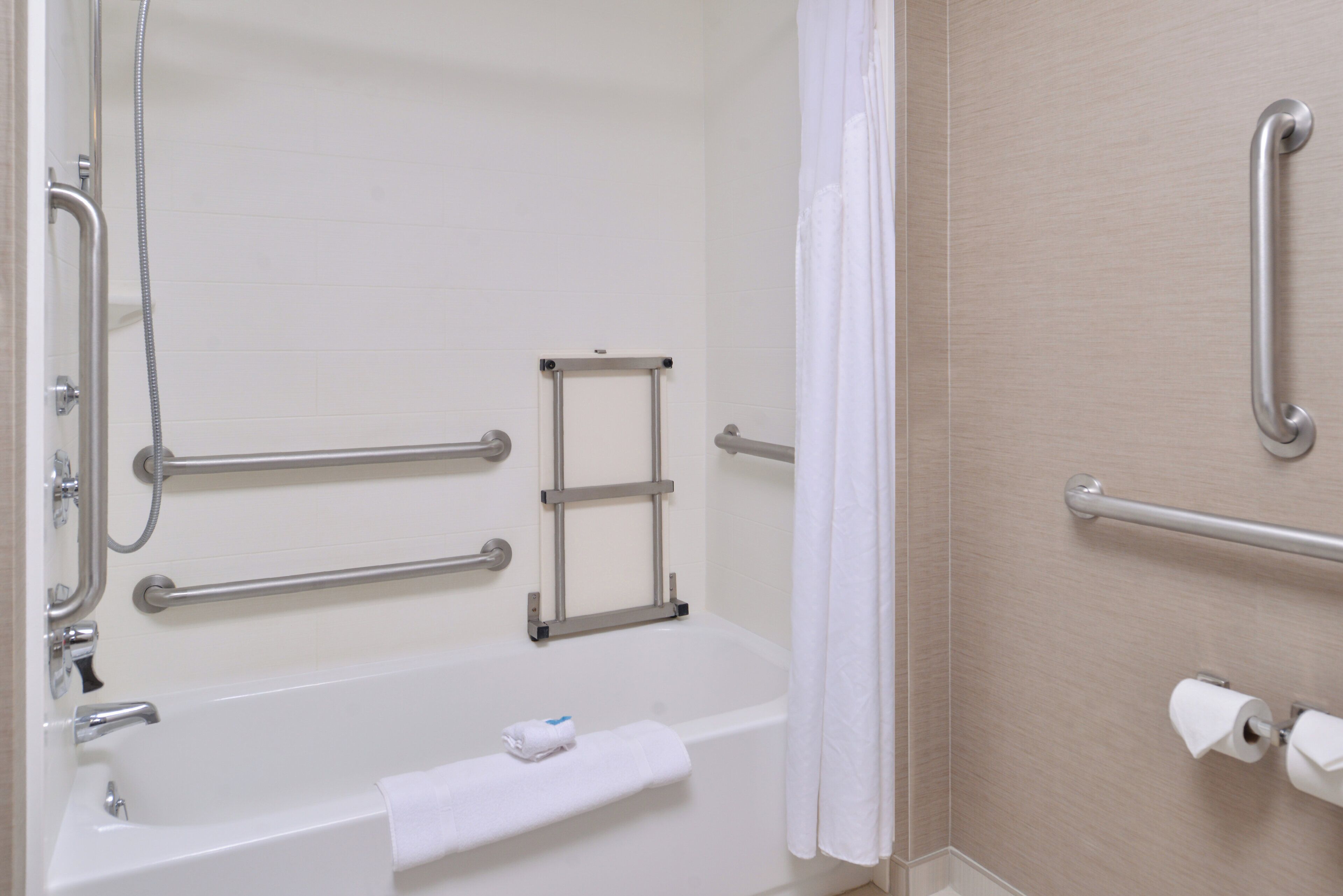 A bathroom with a bathtub, grab bars, a shower, and a toilet paper holder.