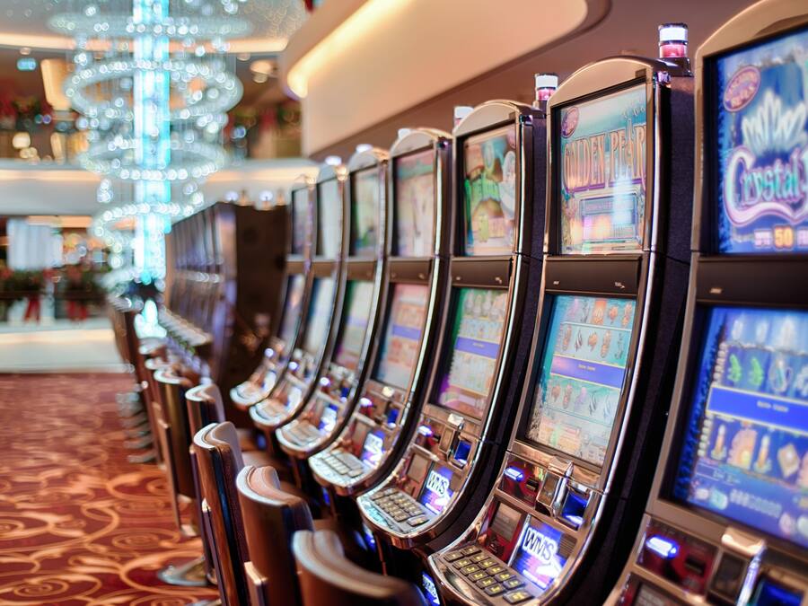 Une rangée de machines à sous dans un casino, avec un lustre en arrière-plan.