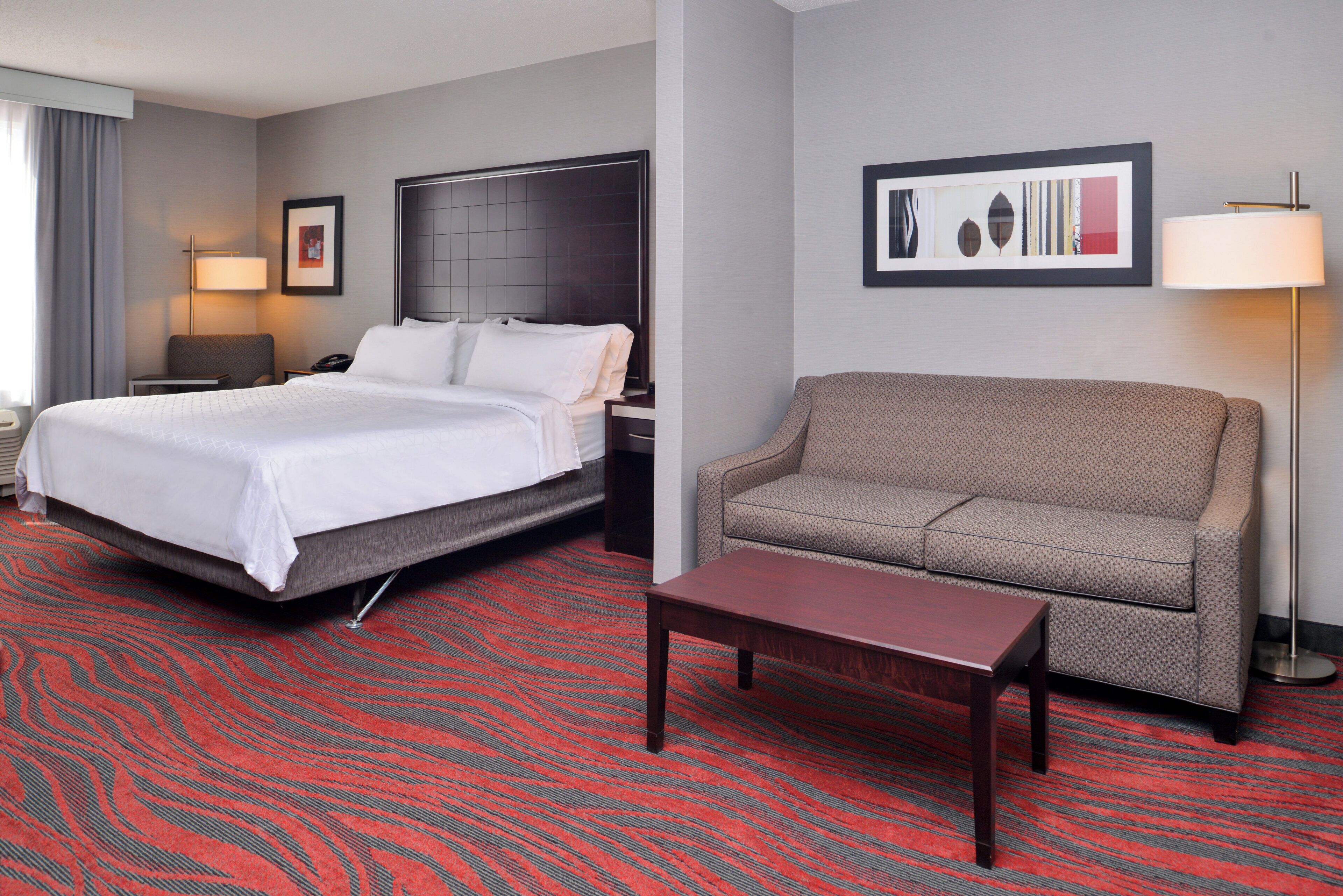 A hotel room with a bed, a sofa, a table, and a lamp.