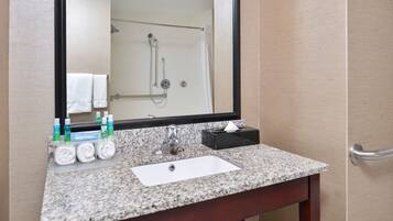 A bathroom with a granite countertop, a white sink, a mirror, and a shower visible in the background.