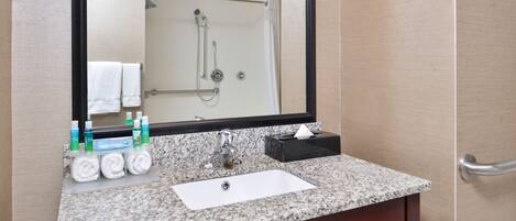 A bathroom with a granite countertop, a white sink, a mirror, and a shower visible in the background.