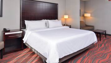 Habitación de hotel con una cama grande, un escritorio con teléfono, una silla y dos lámparas de noche.
