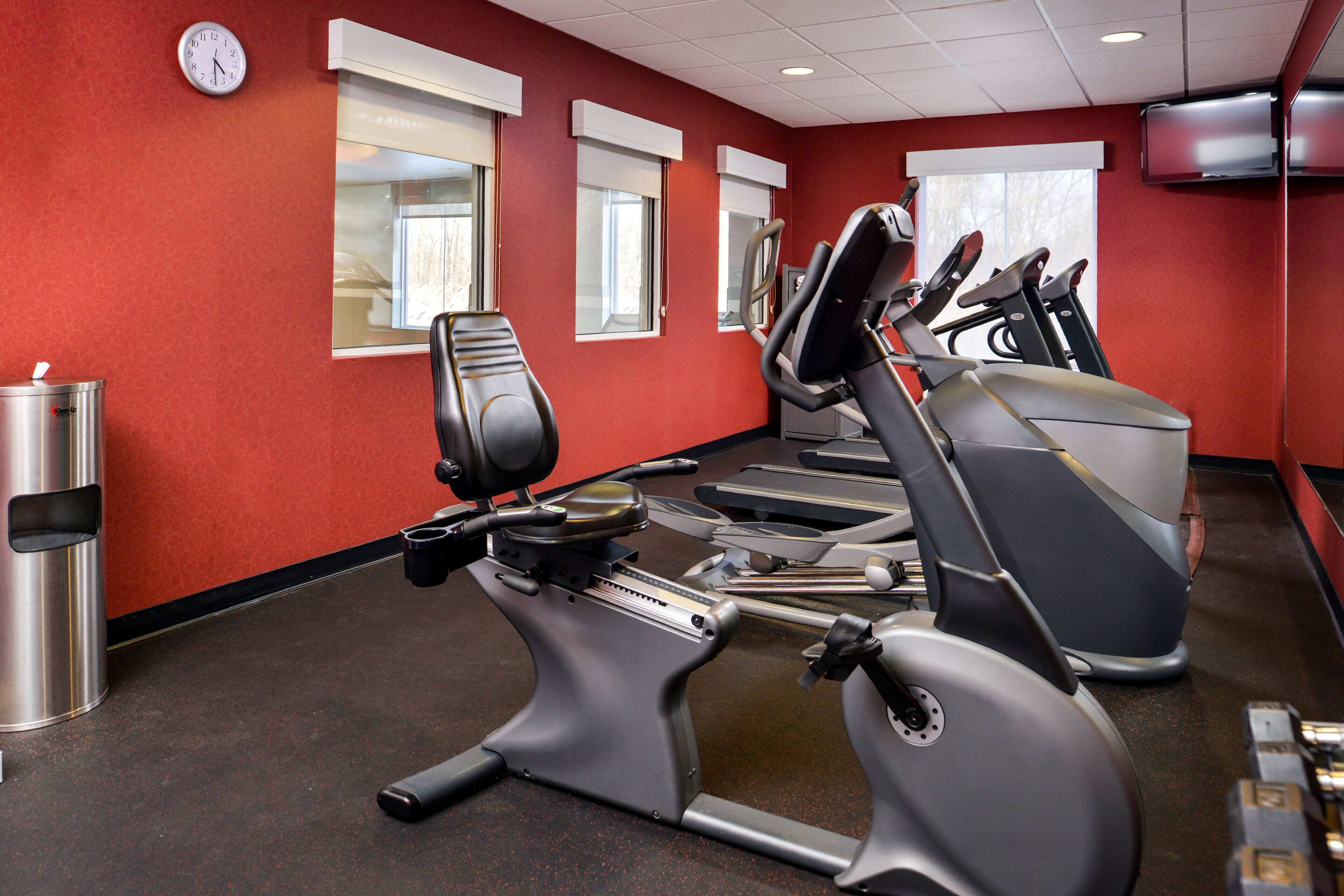 Une salle de sport équipée de matériel d’exercice, avec une horloge et des fenêtres.