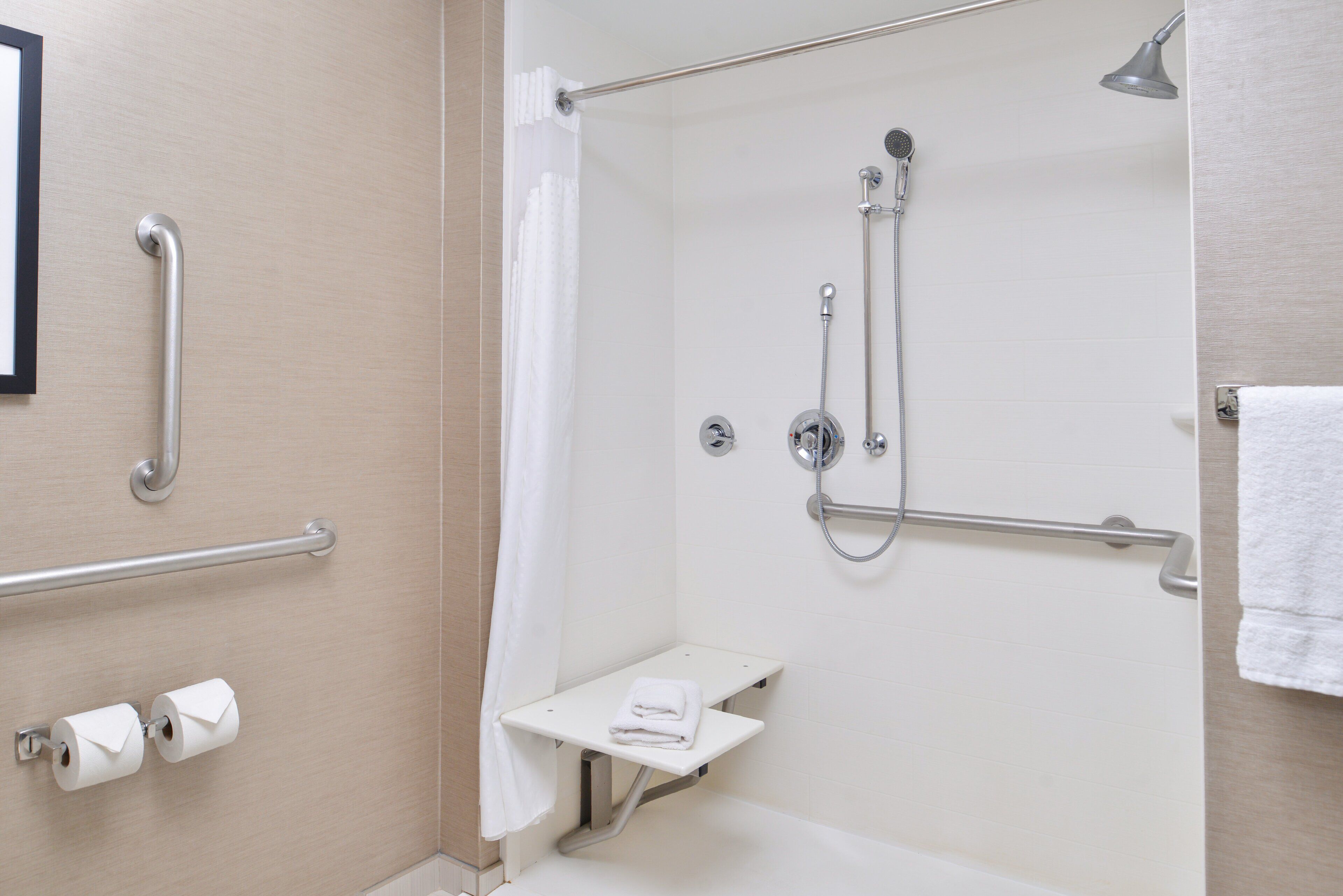 A shower area with a grab bar, a towel rack, and a small shelf with a towel.