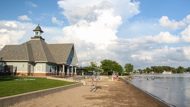 A lakeside building with a dock, a grassy area, and a sandy beach.