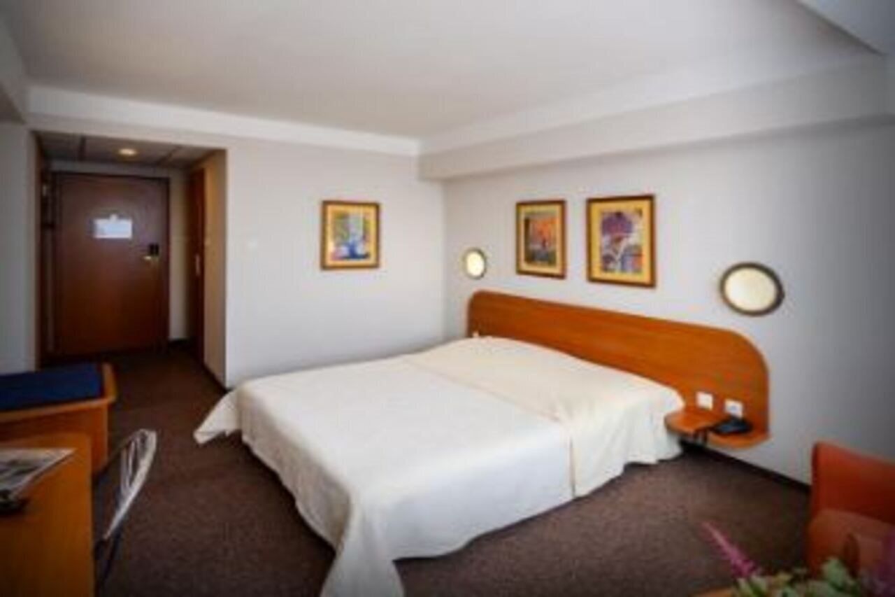 A hotel room with a single bed, a wooden headboard, a desk with a chair, and two framed pictures on the wall.