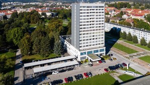A high-rise hotel with multiple floors, a parking lot, and surrounding greenery. - Lux Hotel (Banska Bystrica)