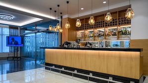 A modern bar area with a wooden counter, hanging light fixtures, and a television screen. - Lux Hotel (Banska Bystrica)