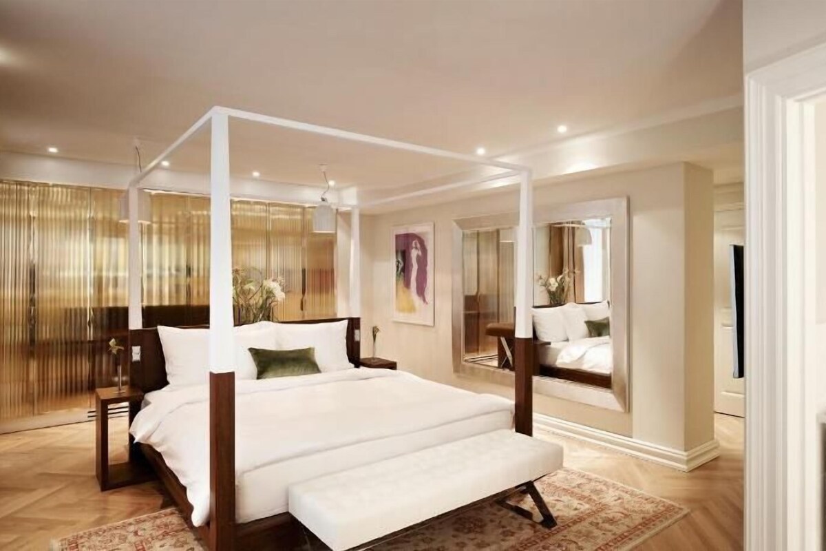 A spacious bedroom with a four-poster bed, a large mirror, and a view of the city.