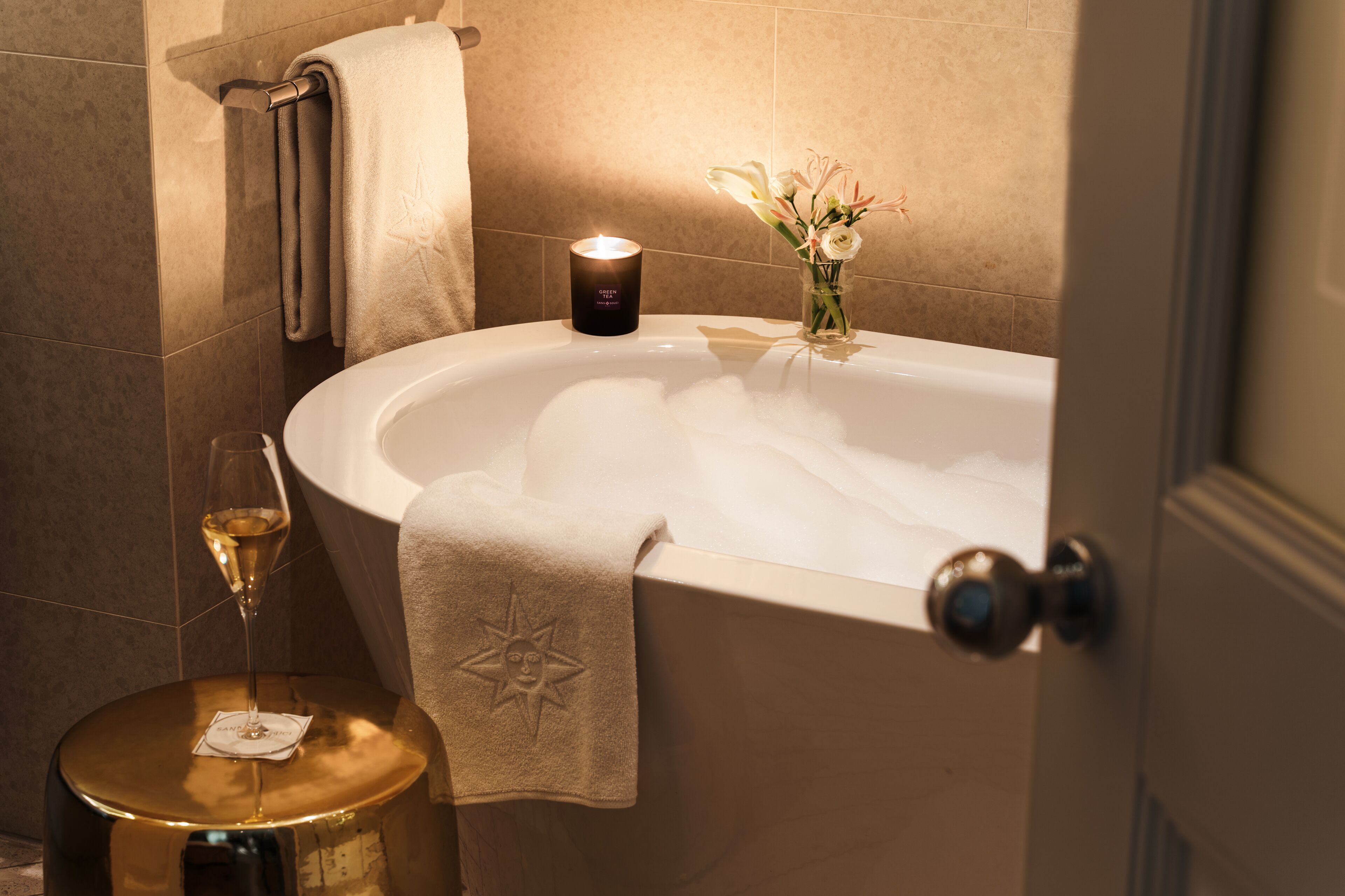 A bathroom with a bathtub, a towel, a glass of wine, and a candle.