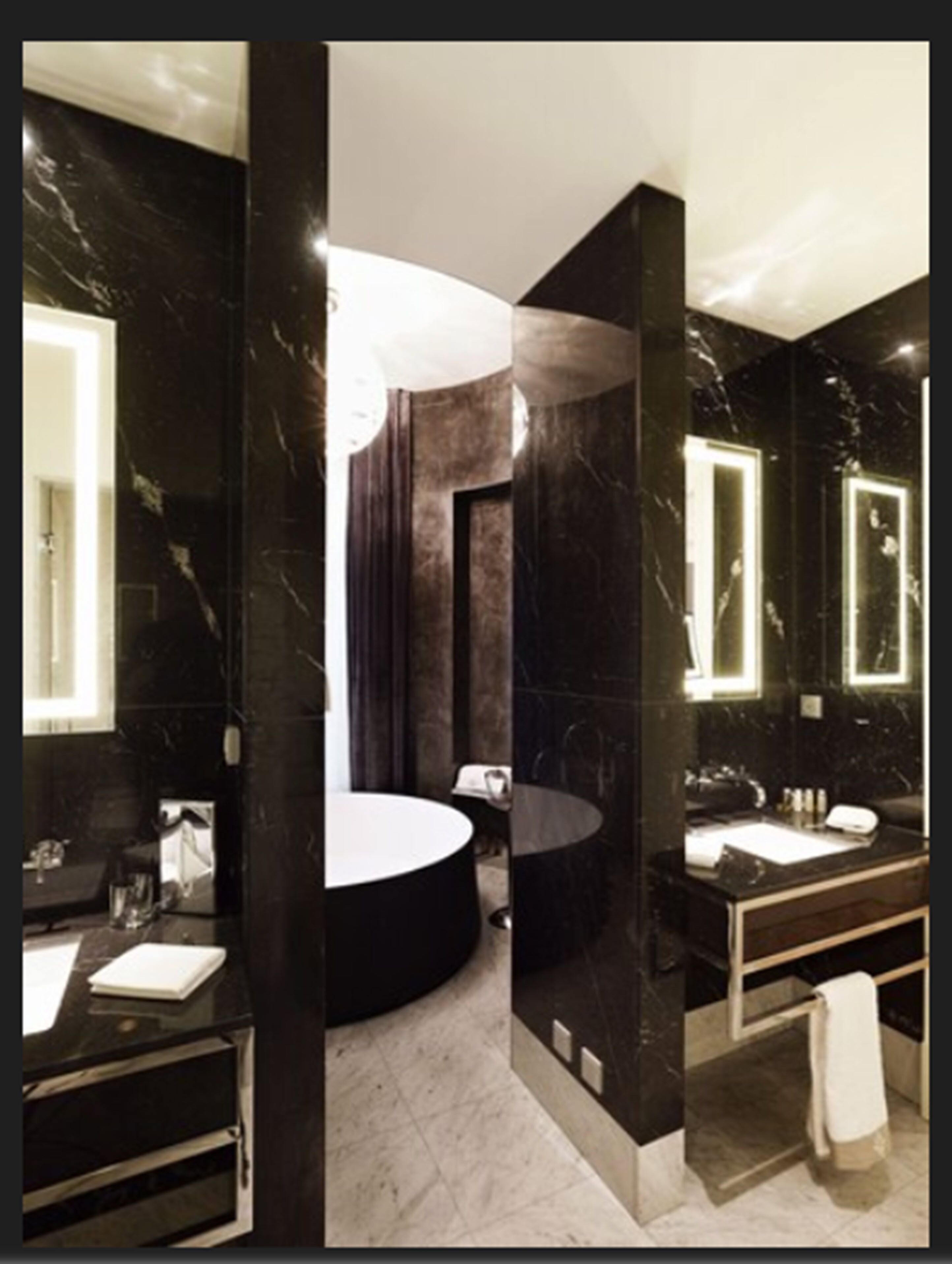 A modern bathroom with a black marble vanity, a round bathtub, and a large mirror.