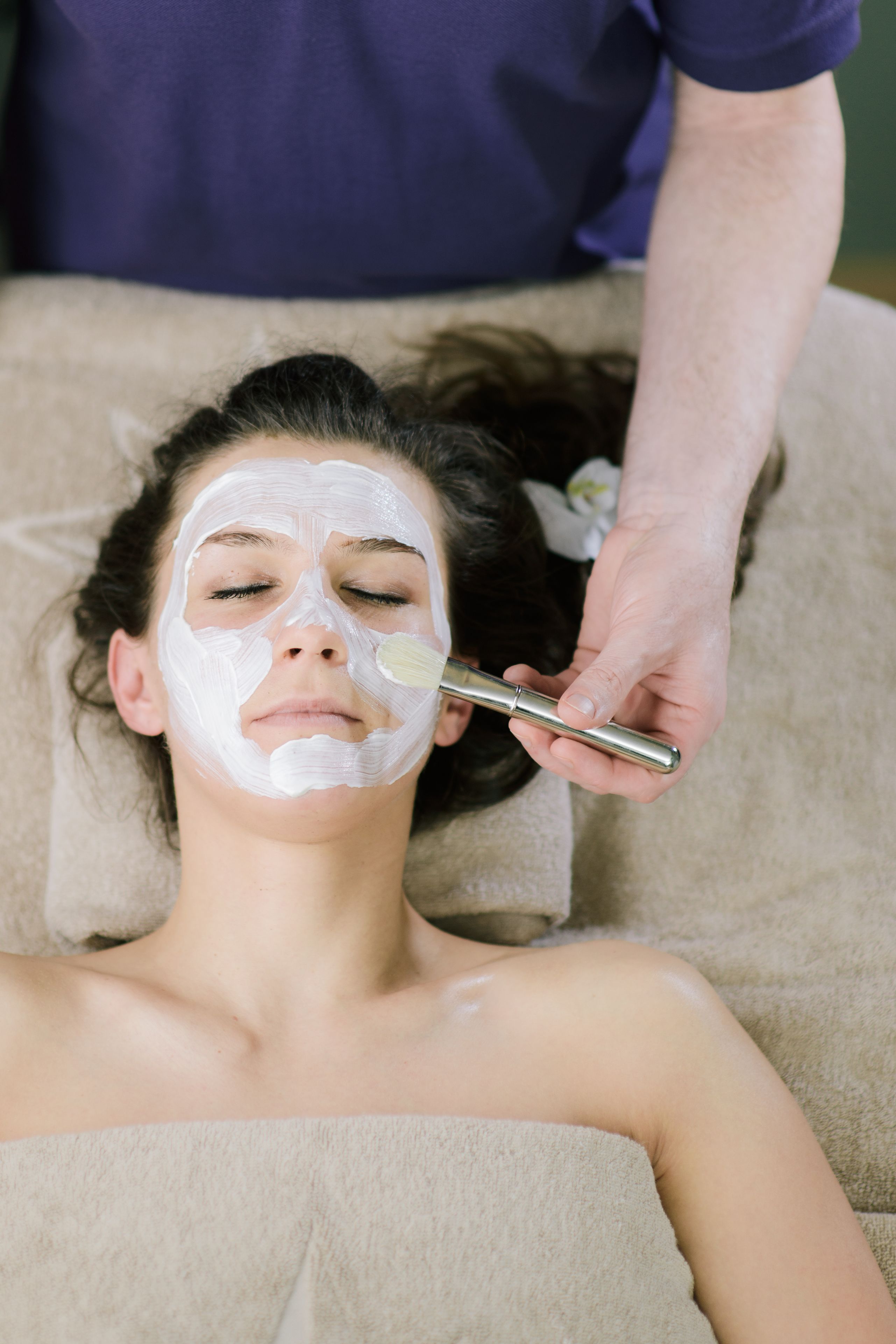 Une personne allongée, une serviette autour du cou, en train de recevoir un soin du visage.