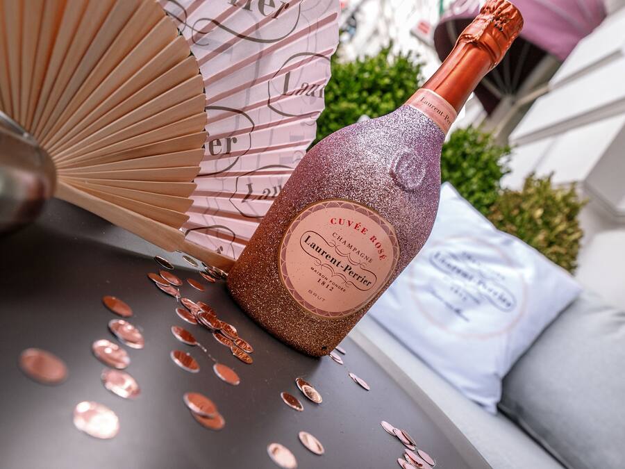 A bottle of Cuvée Rose champagne with a label, placed on a table with scattered champagne glasses.