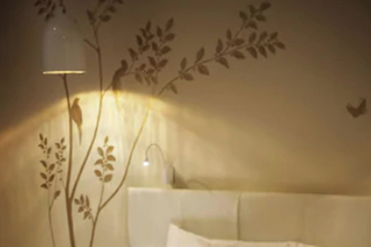 A bed with white bedding, a bedside lamp, and a wall-mounted plant.