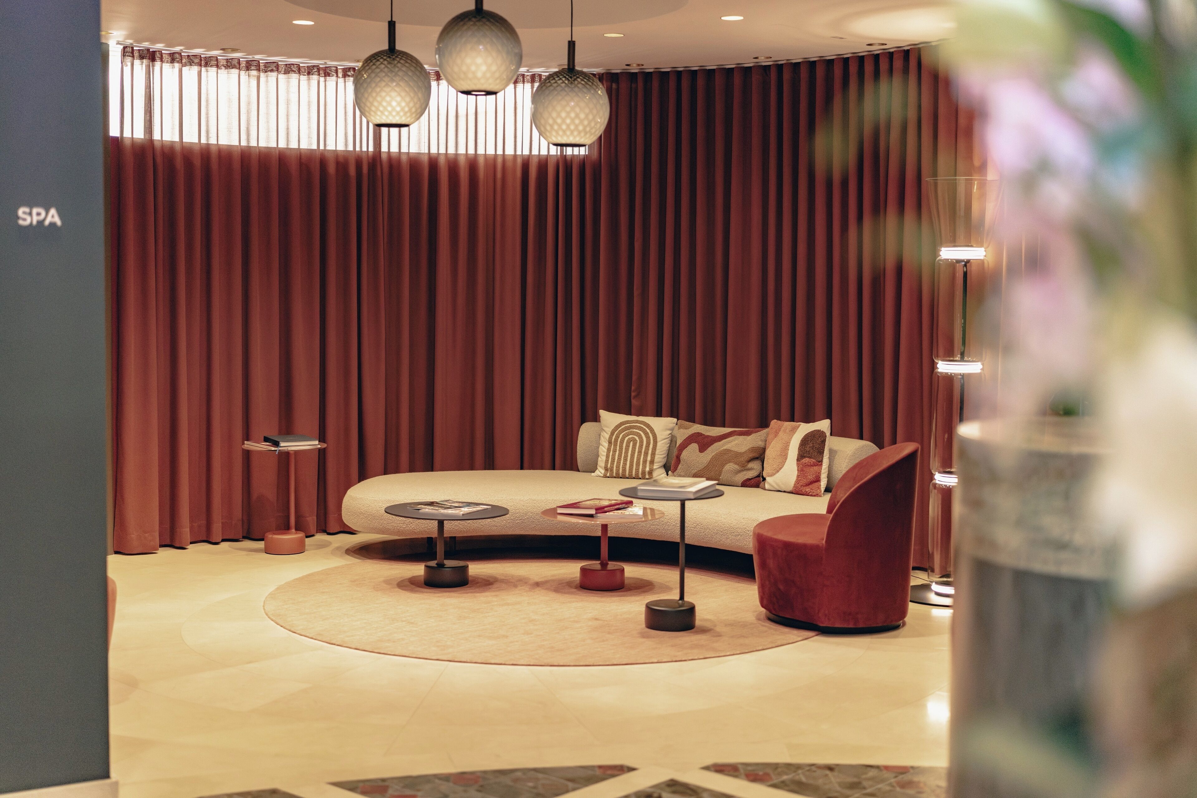 A modern spa room with a curved sofa, round tables, and a large window with curtains.