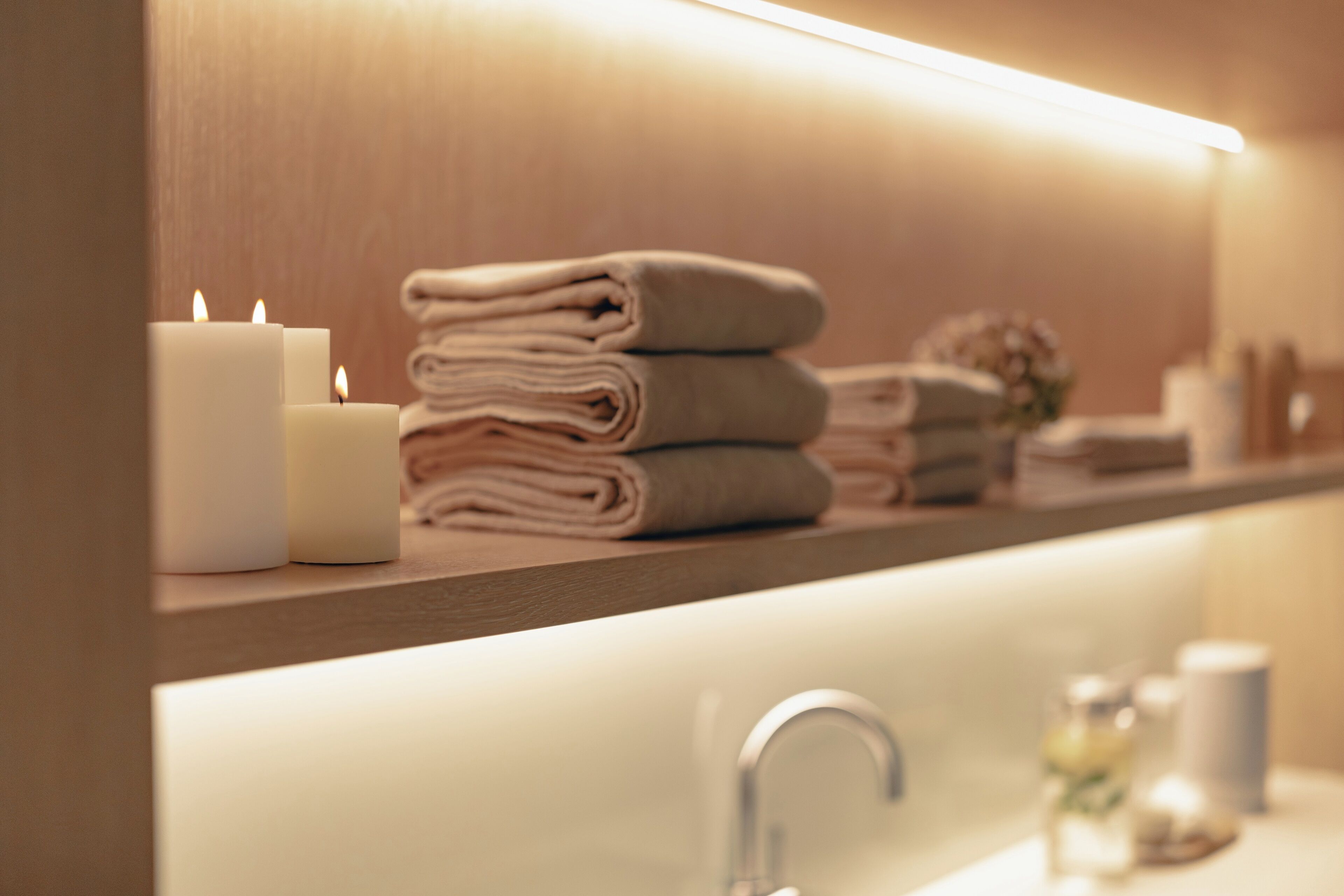 A bathroom with a sink, a mirror, and a shelf with folded towels and candles.