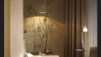 Une chambre avec un lit, une table de chevet, une lampe et un mur orné d’un motif floral.