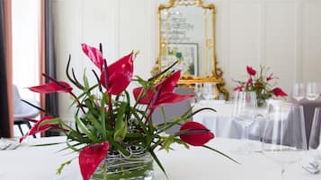 A dining table with a clear glass vase containing red flowers, a gold-framed mirror, and empty wine glasses.