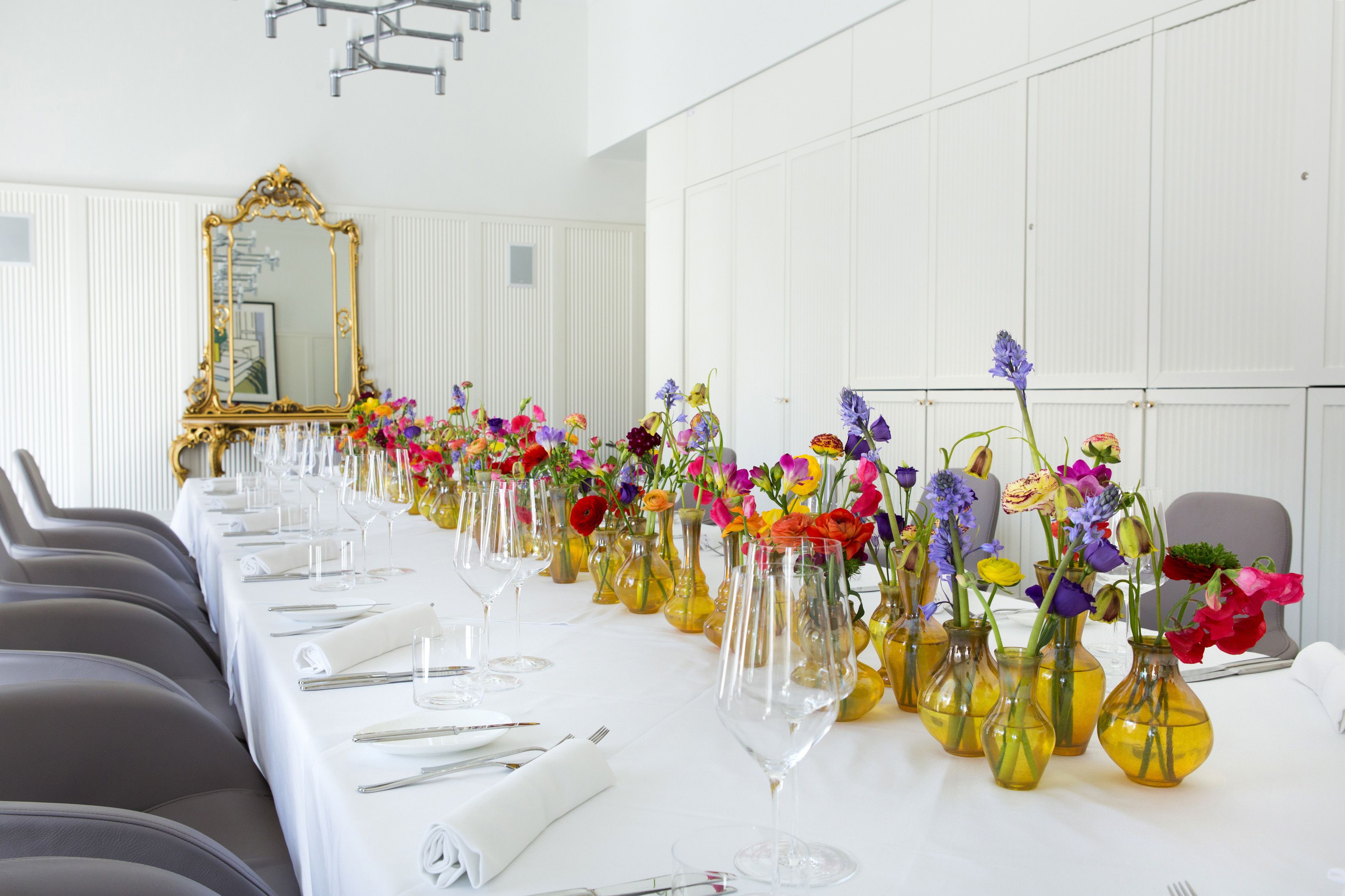 A long dining table with multiple vases of flowers and wine glasses set up for a formal event.