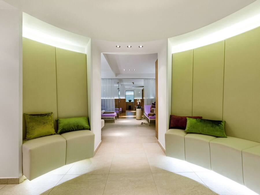 A modern hallway with a curved design, featuring a seating area with green cushions and a view into a dining area.