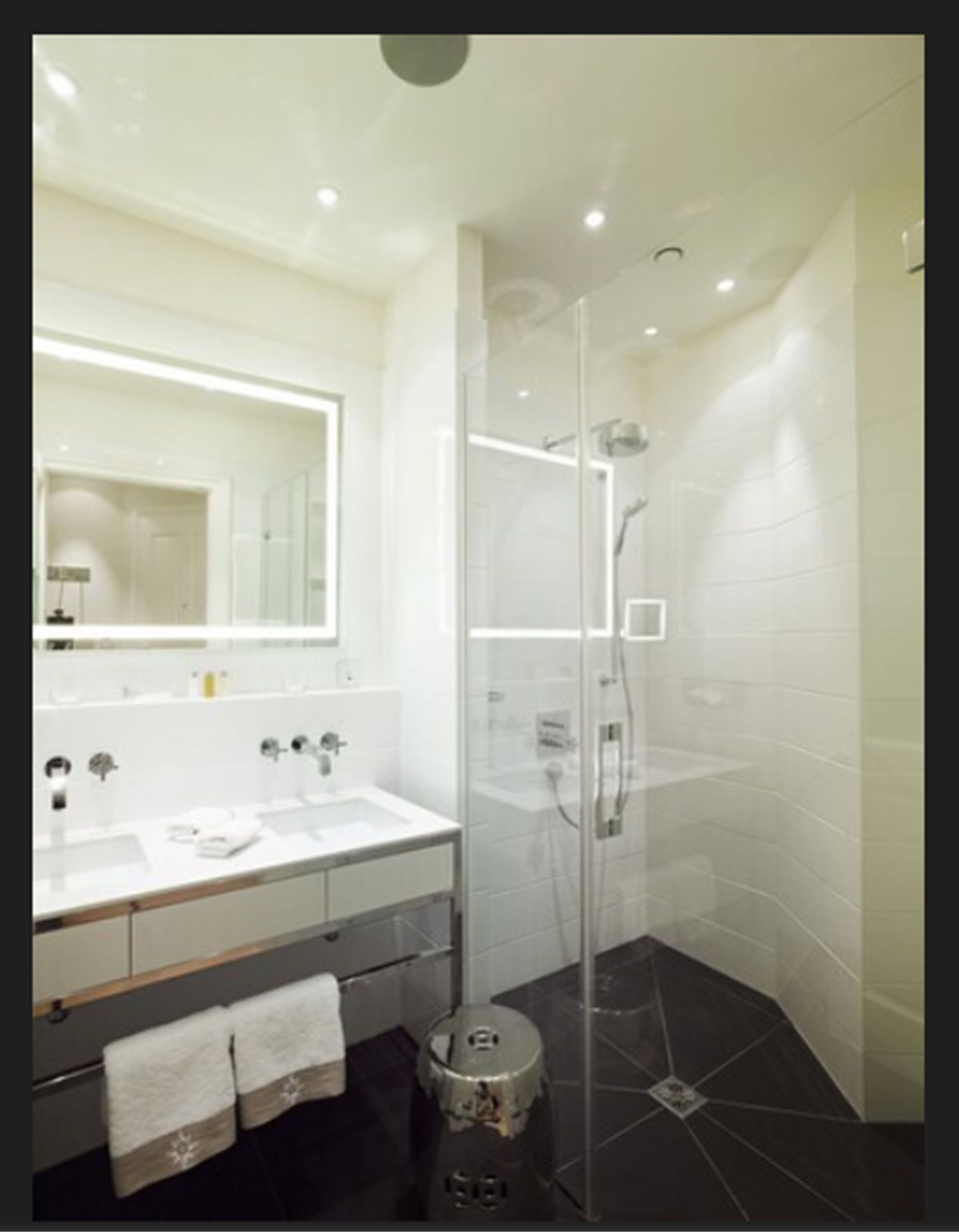 Un baño moderno con ducha envuelta en vidrio, un espejo grande y un tocador blanco con toallero.