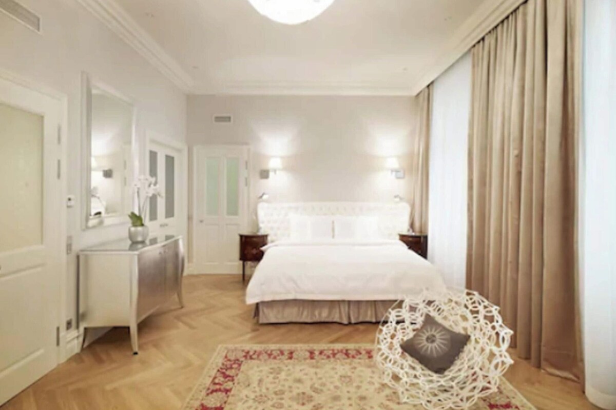 A hotel room with a bed, bedside tables, a dresser, a mirror, and a decorative chair.